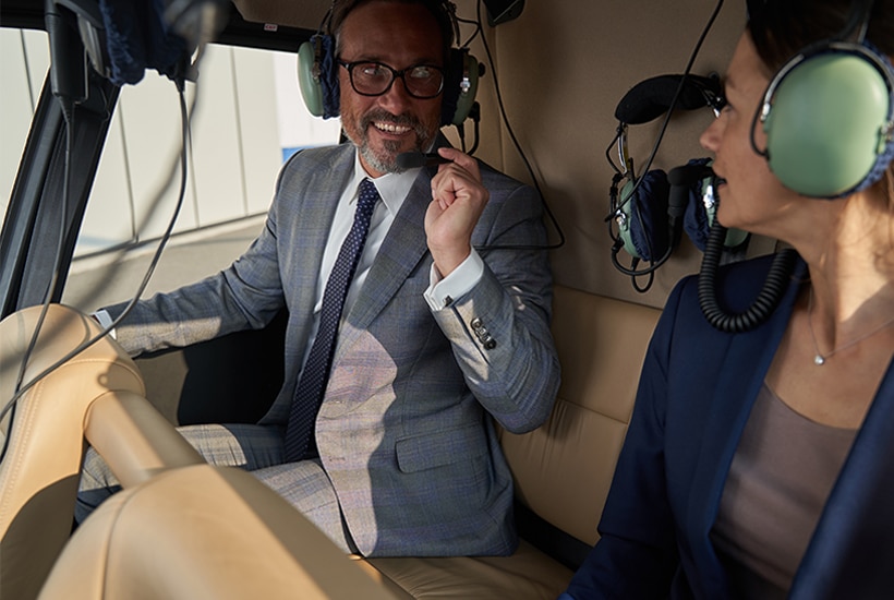 Smiling man in headset speaking to his female travel companion in helicopter cockpit